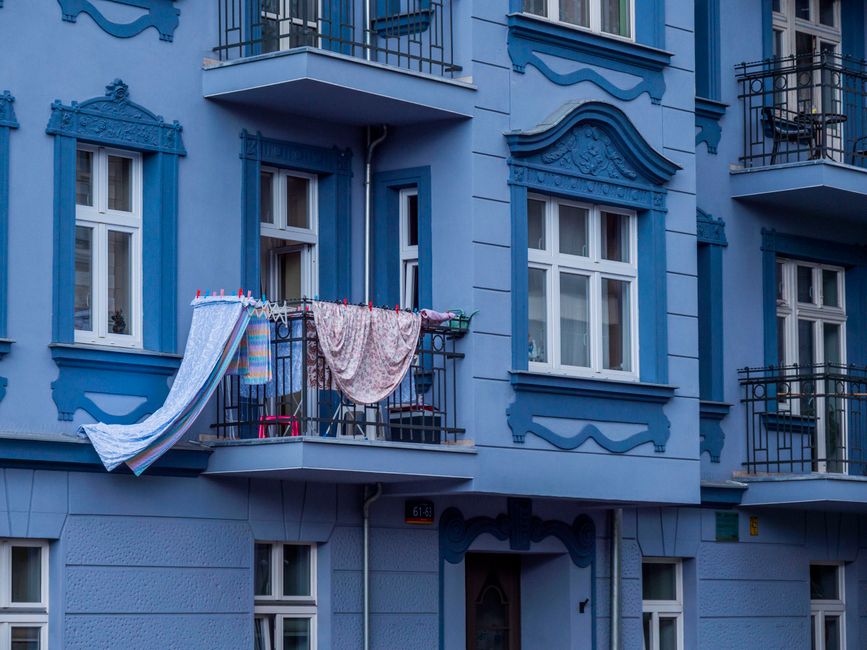 Blue apartment facade with laundry drying on balcony in urban setting.