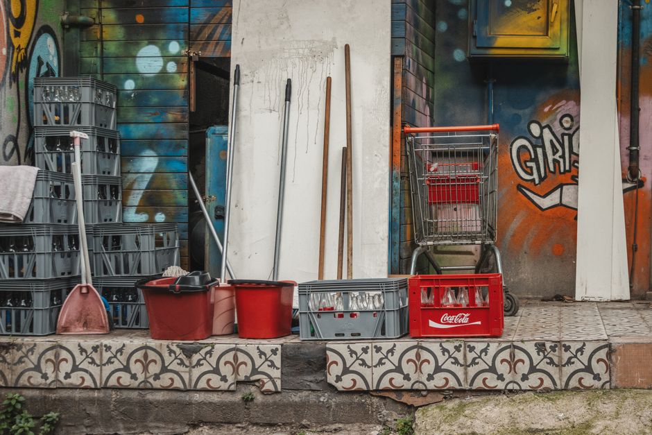 A collection of cleaning supplies and crates set against an artistic, graffiti-covered wall.